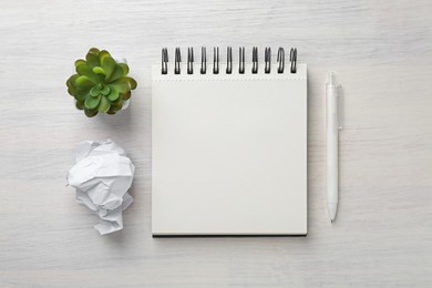 Photo of Notebook, crumpled paper, pen and decorative plant on light wooden table, flat lay