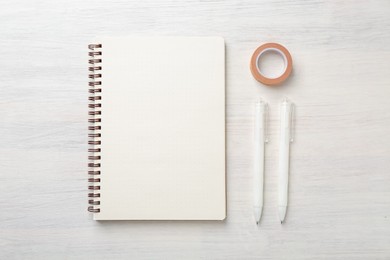 Photo of Notebook, decorative craft tape and pens on light wooden table, flat lay