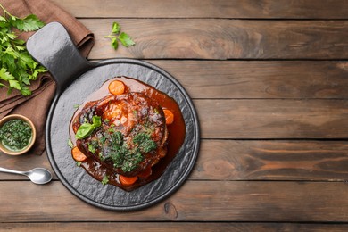 Photo of Traditional ossobuco dish with beef steak and sauce served on wooden table, flat lay. Space for text