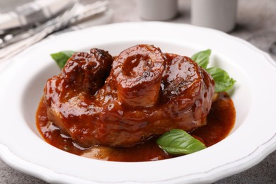 Photo of Traditional ossobuco dish with beef steak, sauce and basil on table, closeup