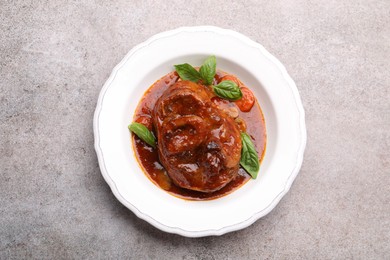Photo of Traditional ossobuco dish with beef steak and sauce on grey table, top view.