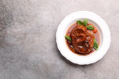 Photo of Traditional ossobuco dish with beef steak and sauce on grey table, top view. Space for text