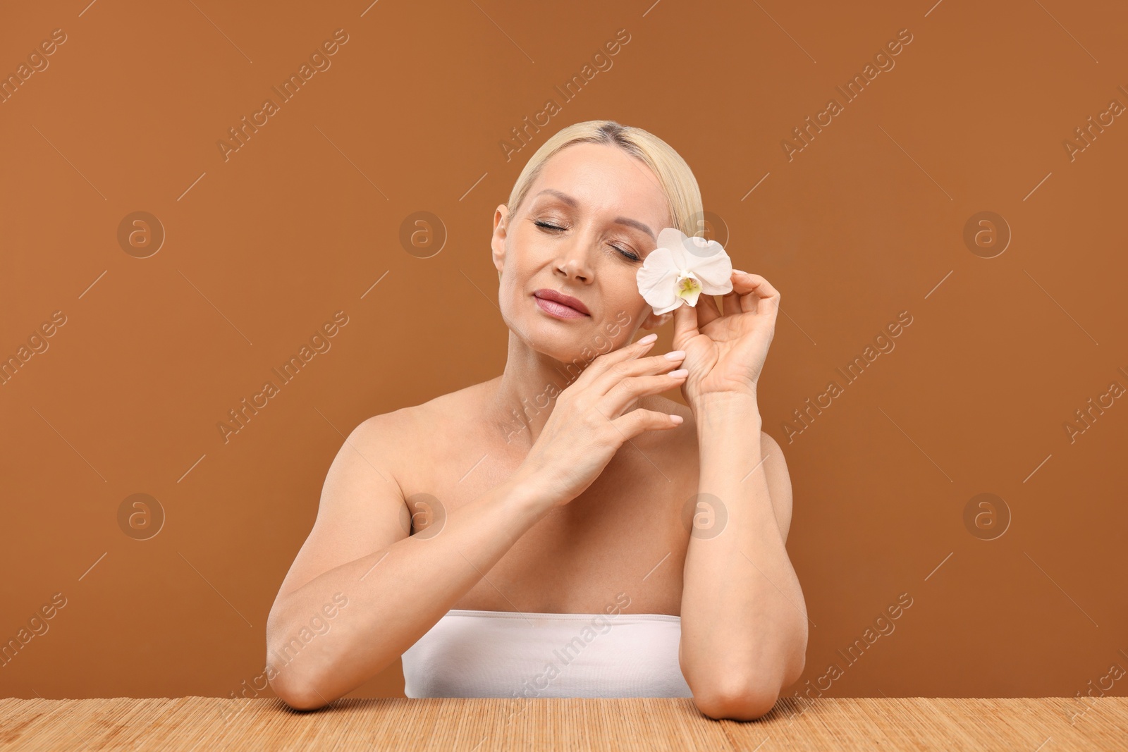 Beautiful woman with orchid flower on brown background Photo of Beautiful woman with orchid flower on brown background