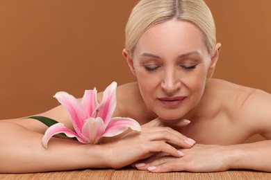 Photo of Beautiful woman with lily flower on brown background, closeup