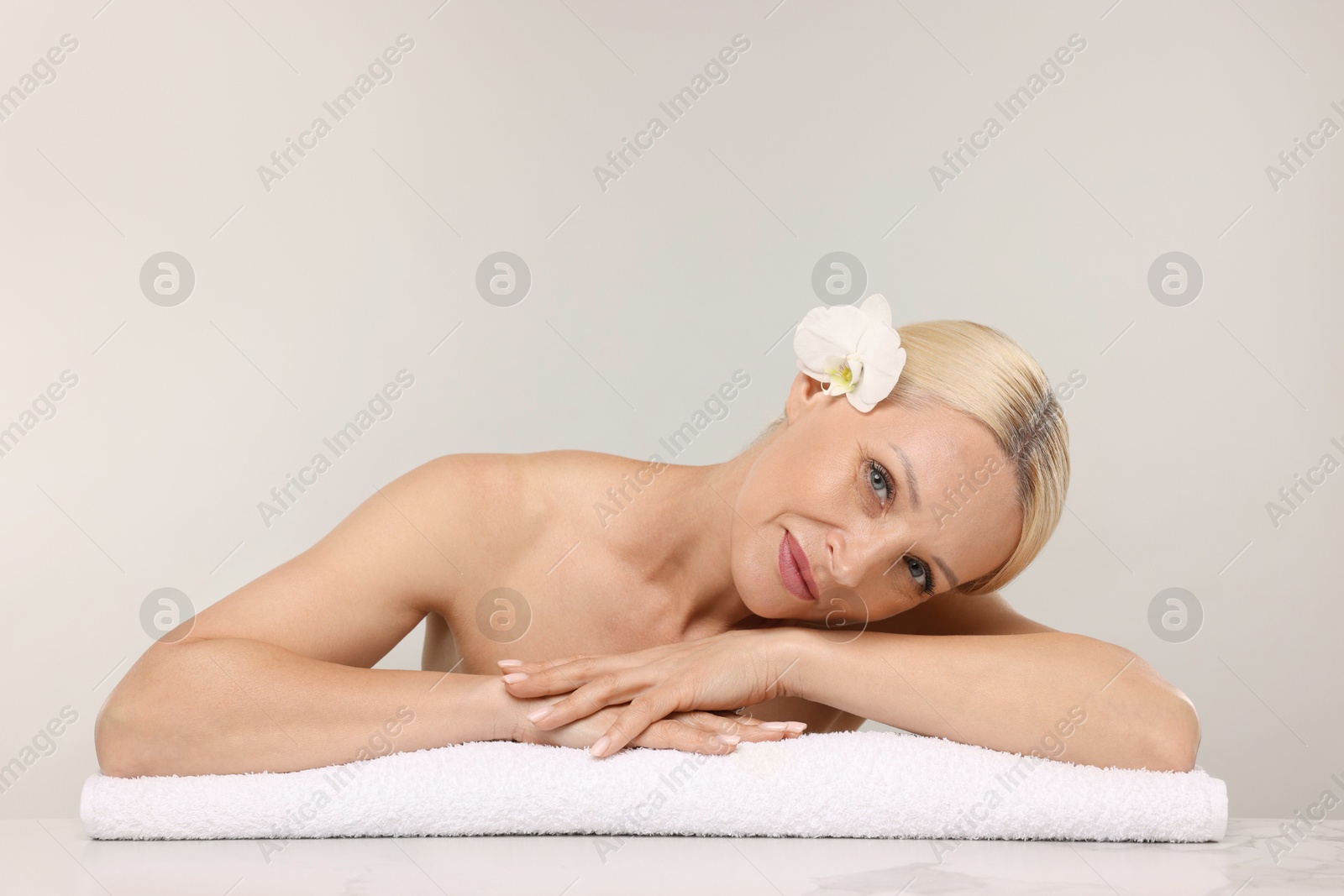 Beautiful woman with orchid flower and towel on light background. Space for text Photo of Beautiful woman with orchid flower and towel on light background. Space for text