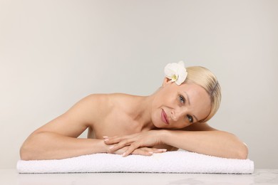 Photo of Beautiful woman with orchid flower and towel on light background. Space for text