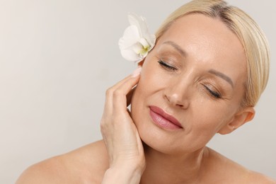 Photo of Beautiful woman with orchid flower on light background, closeup. Space for text