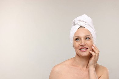 Photo of Beautiful woman with towel wrapped on her head against light background. Space for text