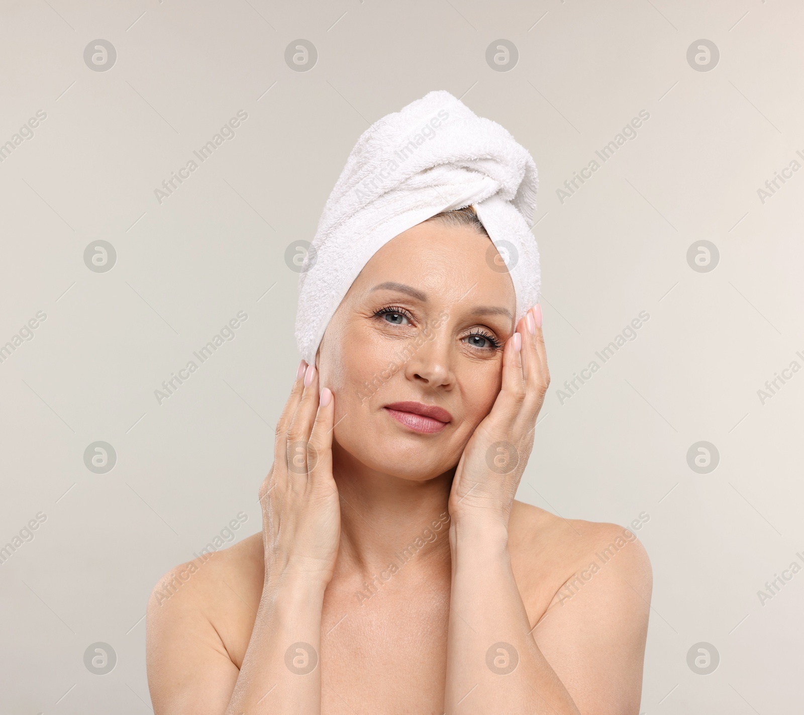 Beautiful woman with towel wrapped on her head against light background Photo of Beautiful woman with towel wrapped on her head against light background