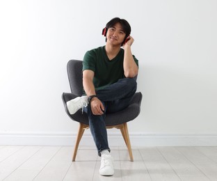 Photo of Handsome Asian man listening to music in headphones on armchair near white wall