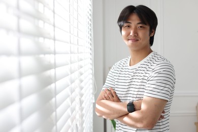 Photo of Portrait of handsome Asian man with crossed arms at home. Space for text