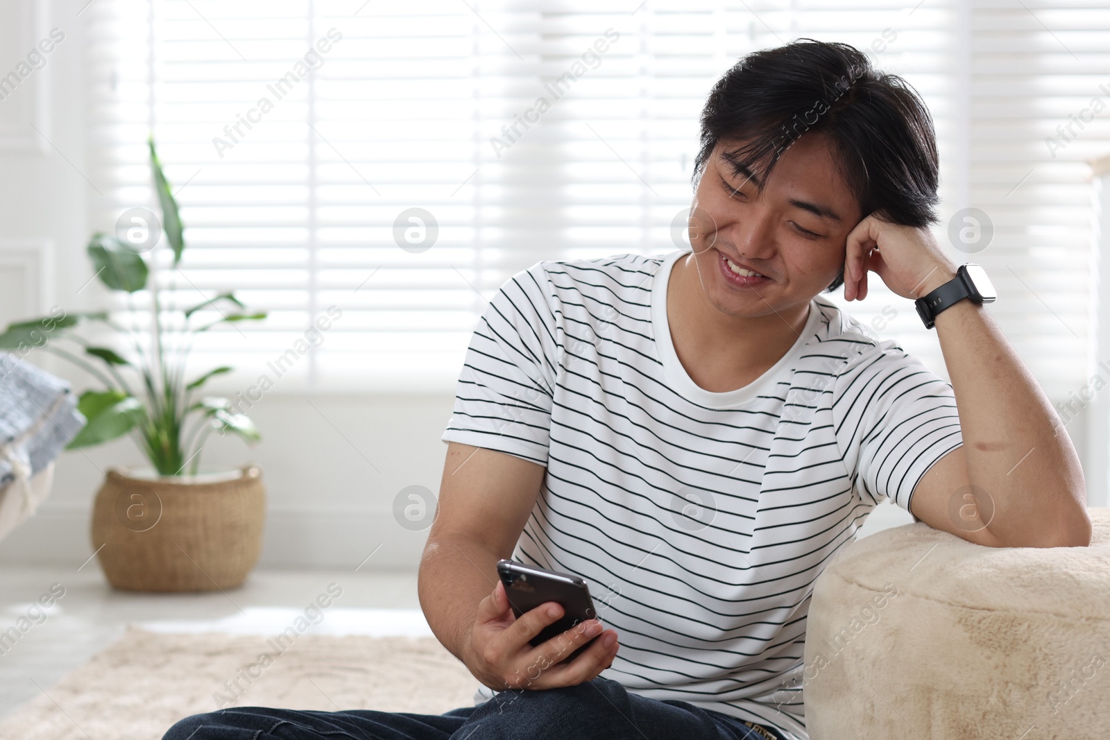 Smiling Asian man with smartphone at home Photo of Smiling Asian man with smartphone at home