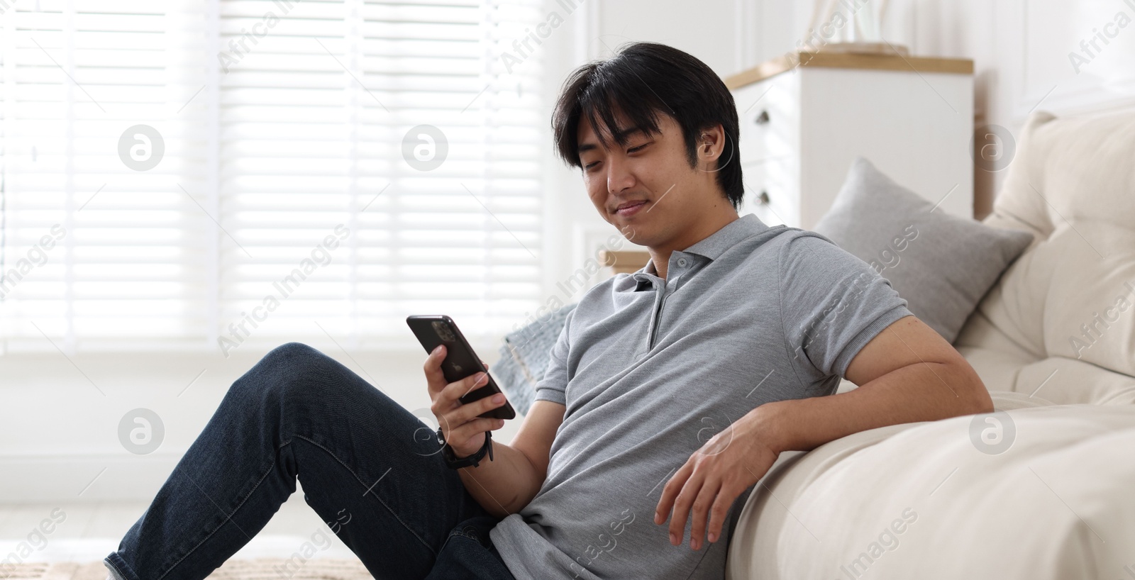 Handsome Asian man with smartphone at home Photo of Handsome Asian man with smartphone at home