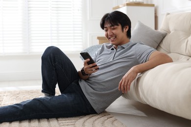 Photo of Smiling Asian man with smartphone on floor at home