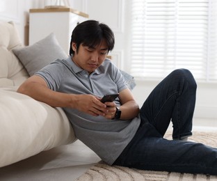 Photo of Handsome Asian man with smartphone on floor at home