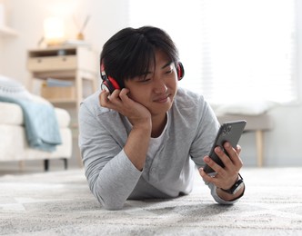 Photo of Handsome Asian man with headphones and smartphone on floor at home