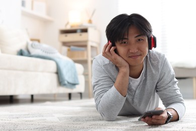 Photo of Handsome Asian man with headphones and smartphone on floor at home. Space for text