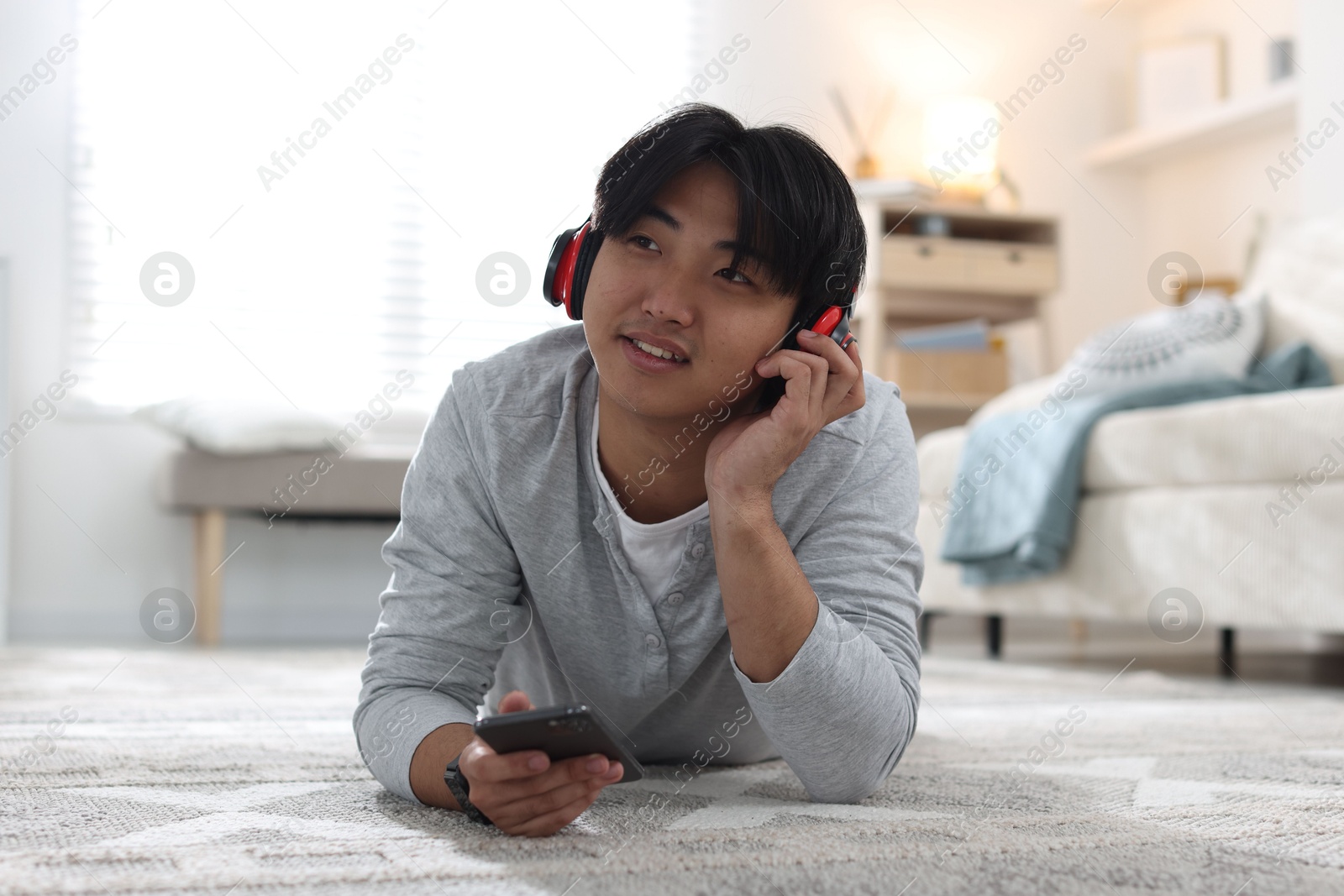 Handsome Asian man with headphones and smartphone on floor at home Photo of Handsome Asian man with headphones and smartphone on floor at home