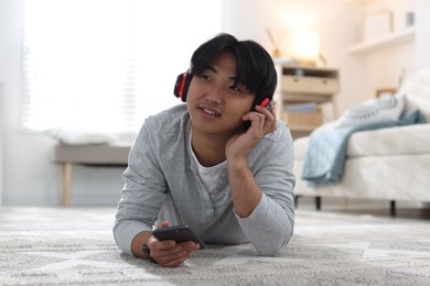 Photo of Handsome Asian man with headphones and smartphone on floor at home