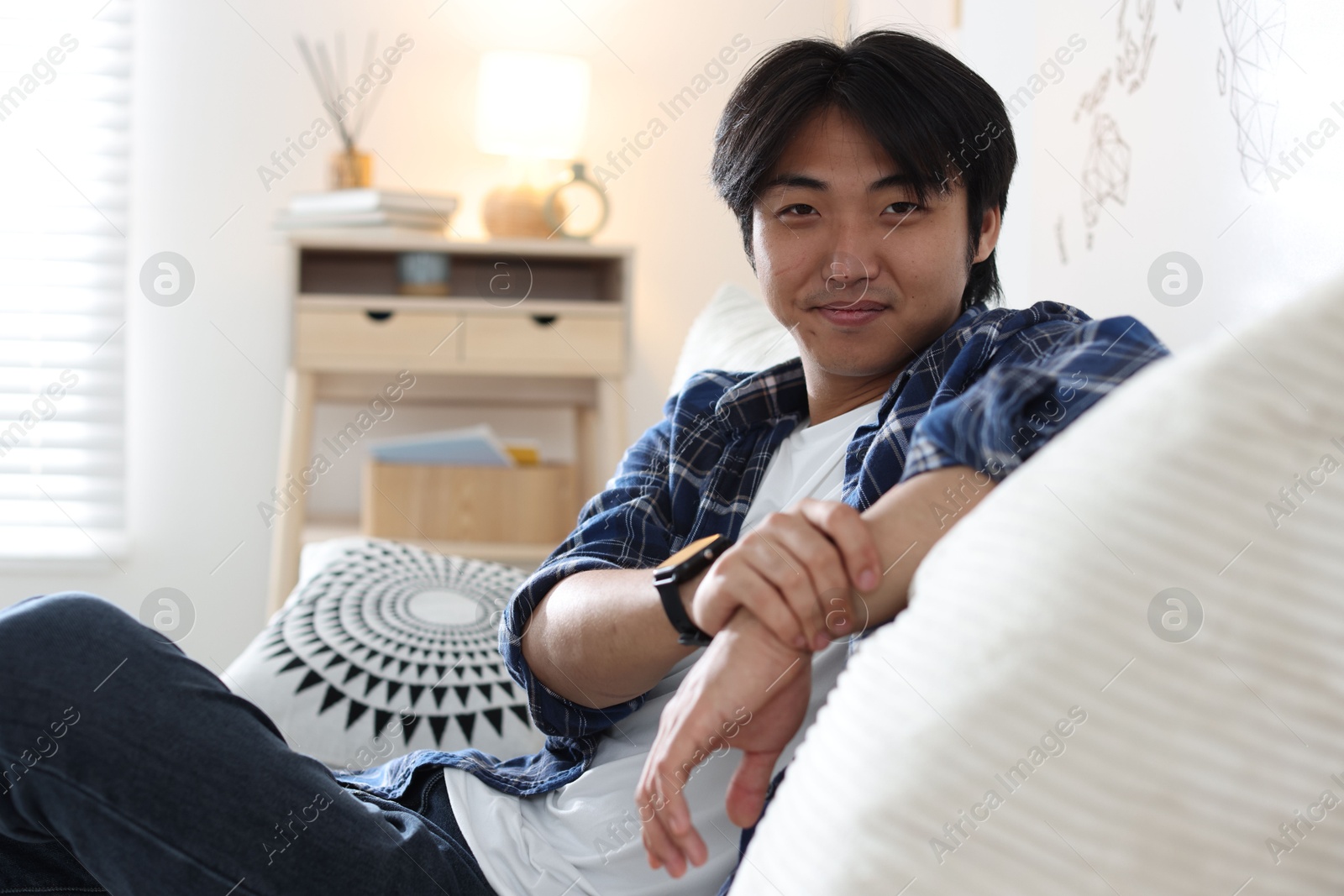 Handsome Asian man sitting on sofa at home Photo of Handsome Asian man sitting on sofa at home