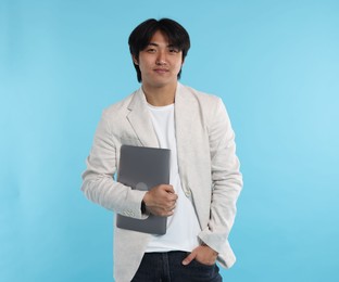 Photo of Handsome Asian businessman in suit with laptop on light blue background