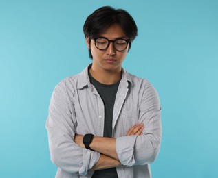Photo of Handsome Asian man in glasses with crossed arms on light blue background