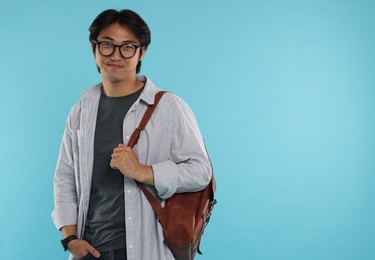 Photo of Handsome Asian man in glasses with backpack on light blue background. Space for text