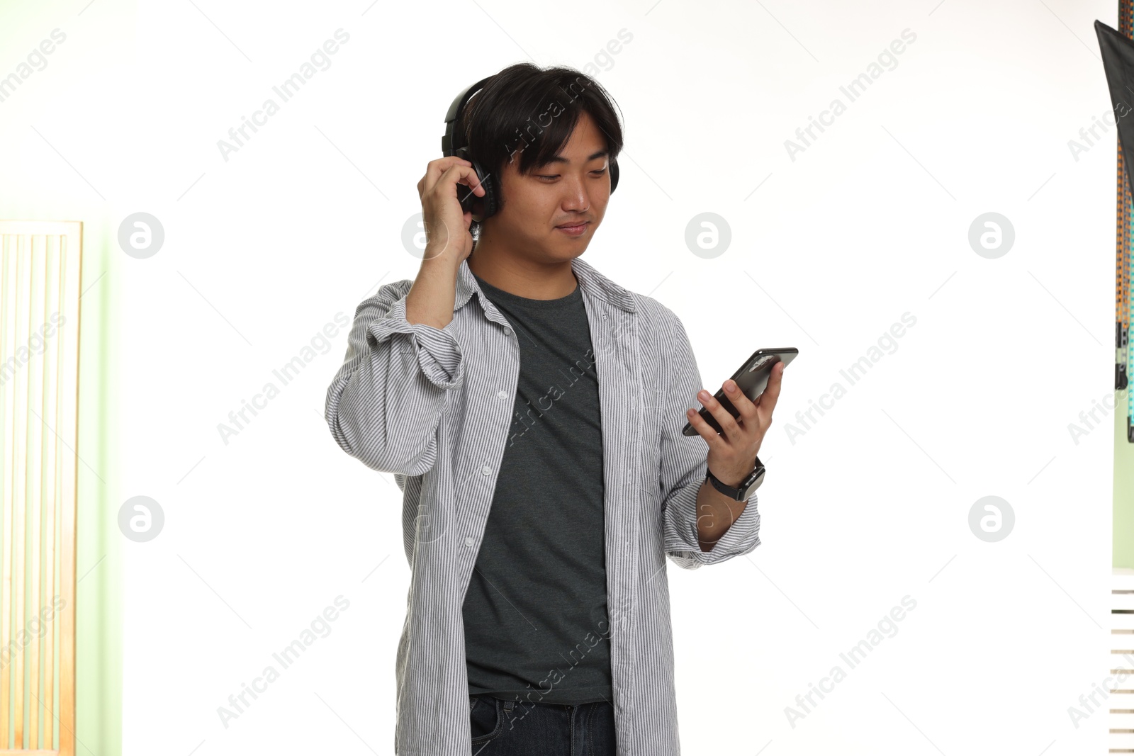 Handsome Asian man in headphones with smartphone on white background Photo of Handsome Asian man in headphones with smartphone on white background