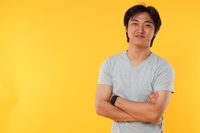 Photo of Portrait of handsome Asian man with crossed arms on yellow background. Space for text