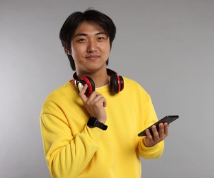Photo of Handsome Asian man with headphones and smartphone on grey background