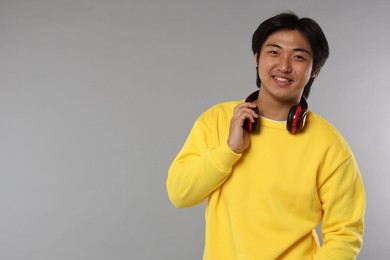 Photo of Smiling Asian man with headphones on grey background. Space for text