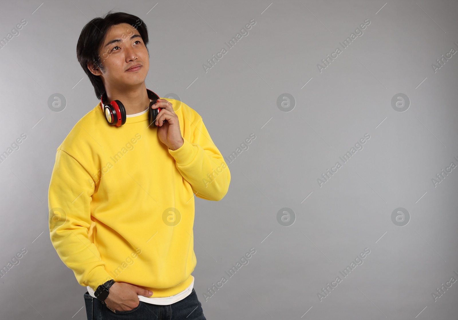 Handsome Asian man with headphones on grey background. Space for text Photo of Handsome Asian man with headphones on grey background. Space for text