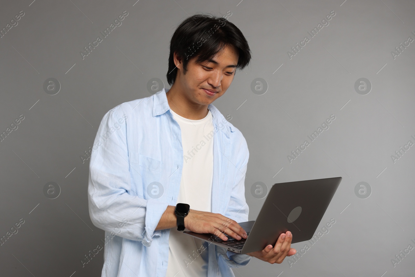 Handsome Asian man with laptop on grey background Photo of Handsome Asian man with laptop on grey background