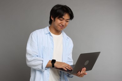 Photo of Handsome Asian man with laptop on grey background