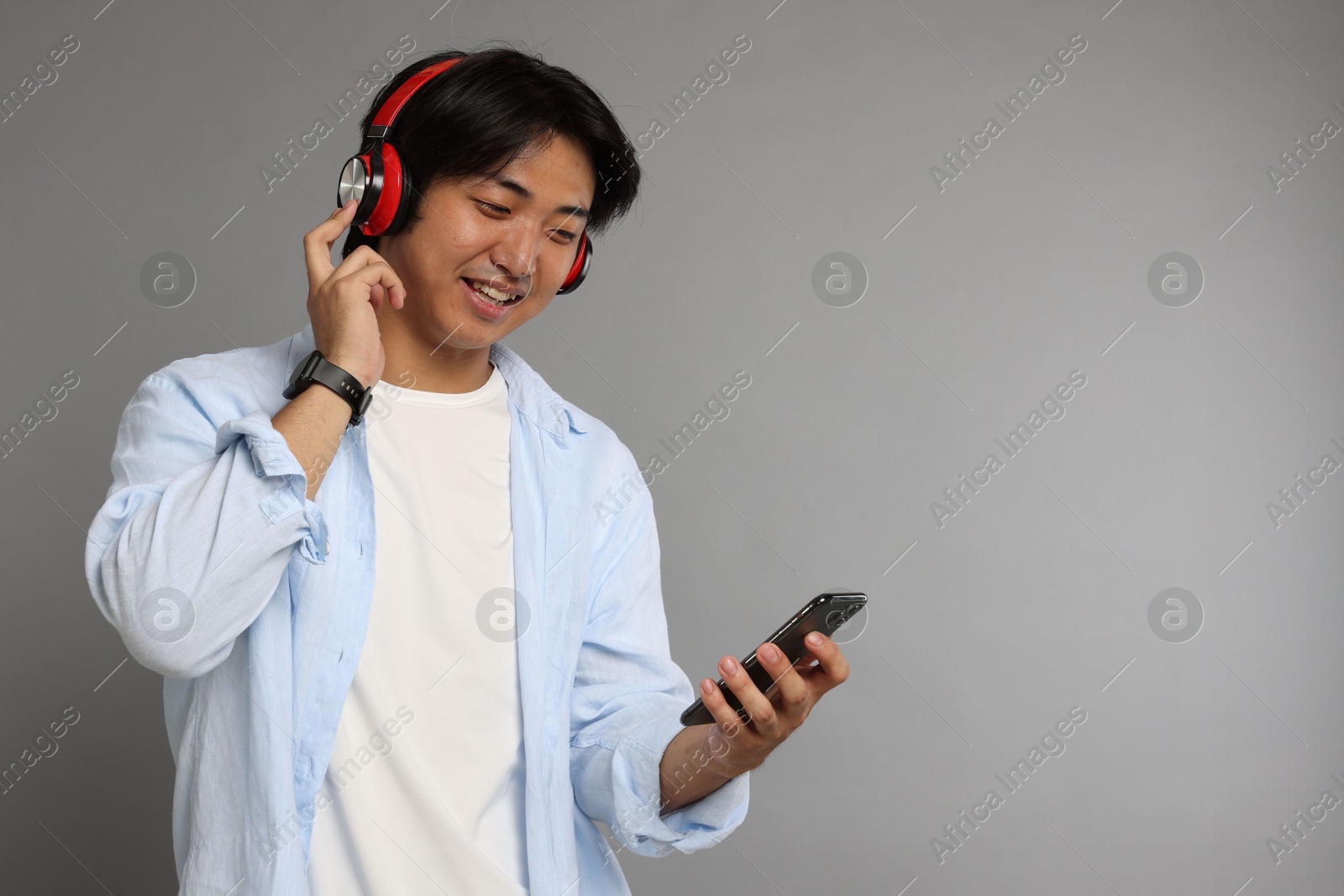 Smiling Asian man in headphones with smartphone on grey background. Space for text Photo of Smiling Asian man in headphones with smartphone on grey background. Space for text