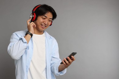 Photo of Smiling Asian man in headphones with smartphone on grey background. Space for text