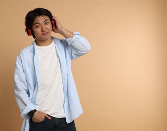 Photo of Handsome Asian man in headphones on beige background. Space for text