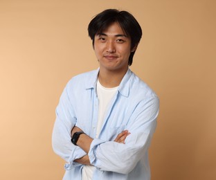 Photo of Portrait of handsome Asian man with crossed arms on beige background