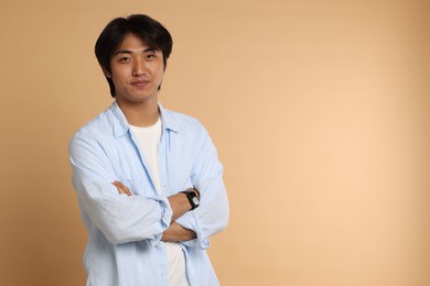 Photo of Portrait of handsome Asian man with crossed arms on beige background. Space for text