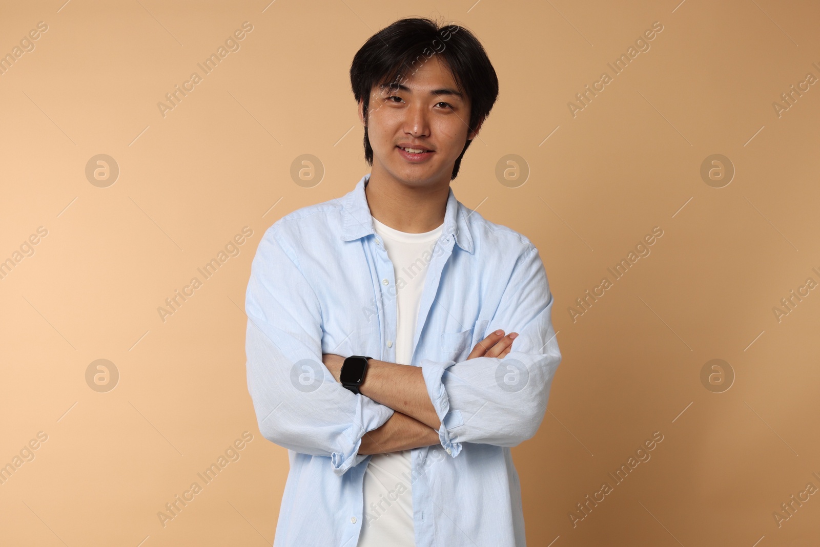 Portrait of smiling Asian man with crossed arms on beige background Photo of Portrait of smiling Asian man with crossed arms on beige background