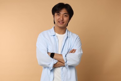 Photo of Portrait of smiling Asian man with crossed arms on beige background