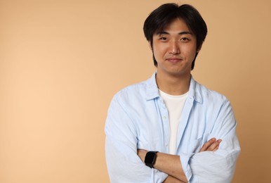 Photo of Portrait of handsome Asian man with crossed arms on beige background. Space for text