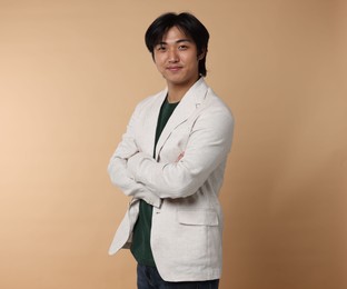 Photo of Portrait of handsome Asian businessman in suit with crossed arms on beige background