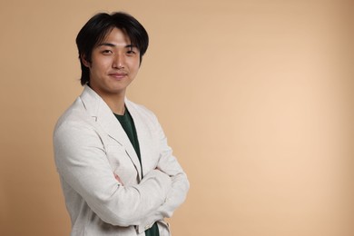 Photo of Portrait of handsome Asian businessman in suit with crossed arms on beige background. Space for text