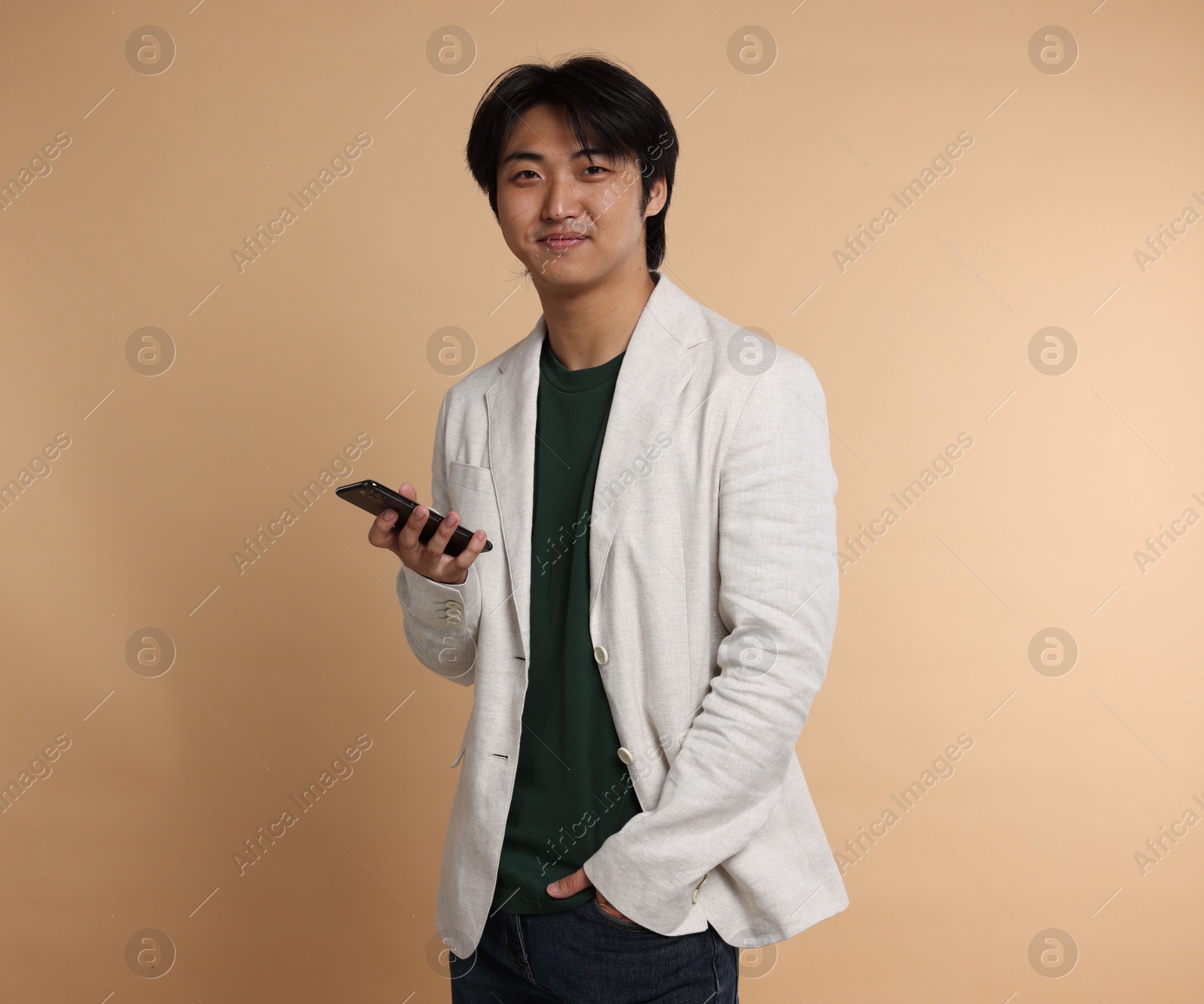 Portrait of handsome Asian businessman in suit with smartphone on beige background Photo of Portrait of handsome Asian businessman in suit with smartphone on beige background