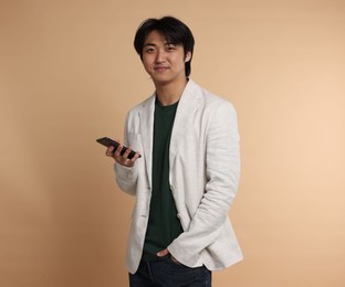 Photo of Portrait of handsome Asian businessman in suit with smartphone on beige background