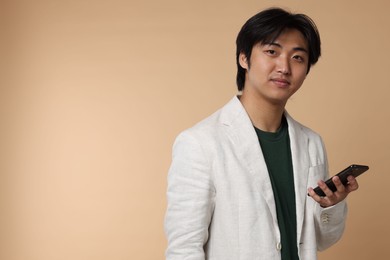 Photo of Portrait of handsome Asian businessman in suit with smartphone on beige background. Space for text