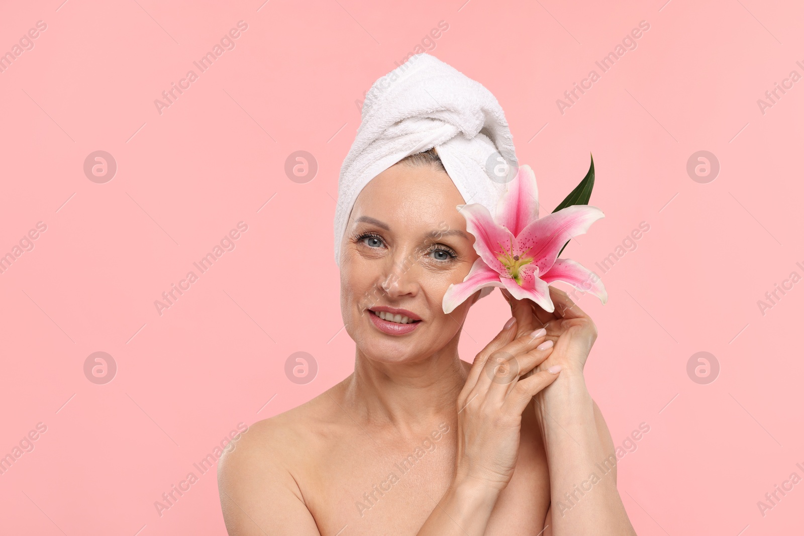 Beautiful woman with flower and towel wrapped on her head against light pink background Photo of Beautiful woman with flower and towel wrapped on her head against light pink background