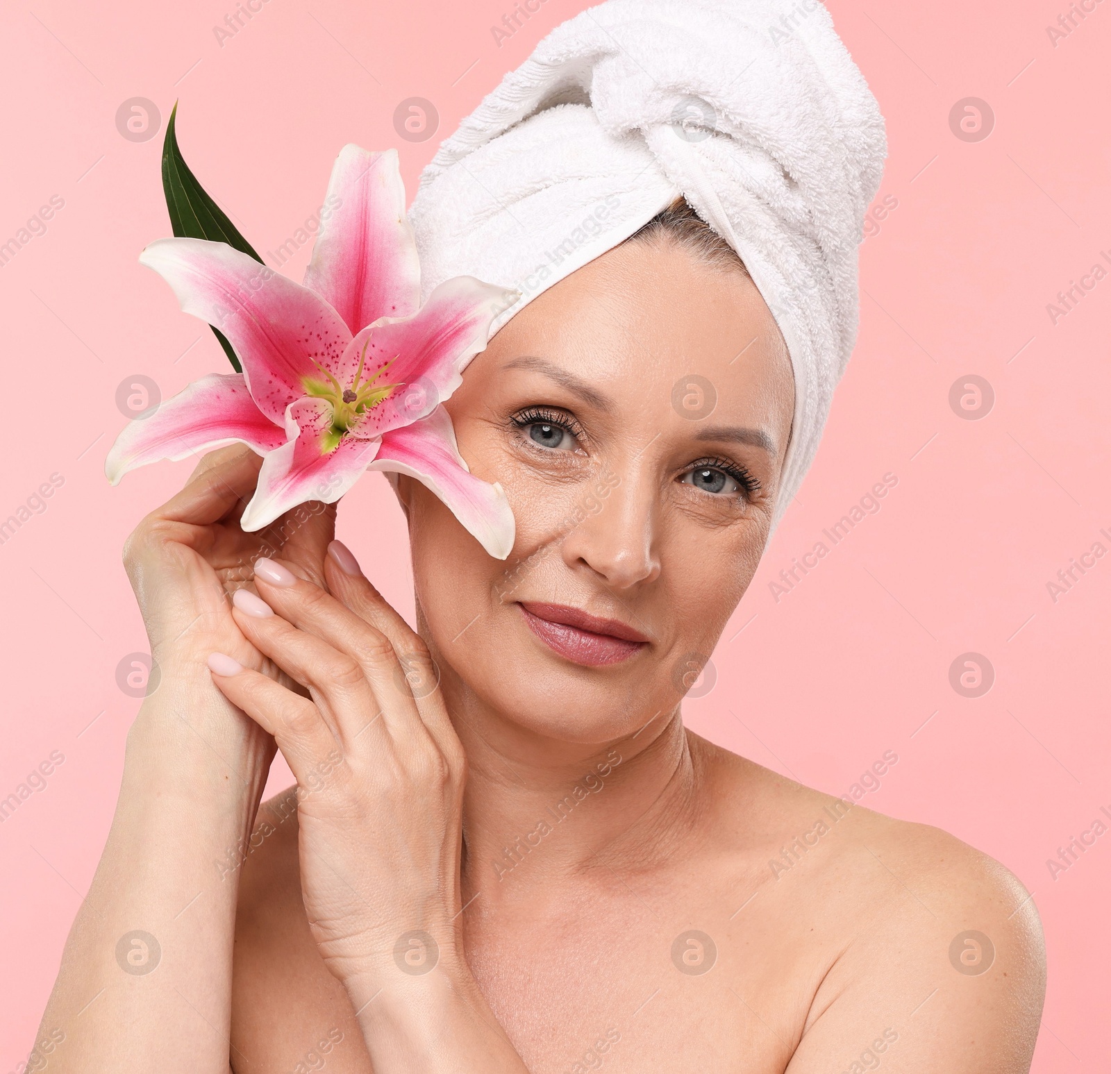 Beautiful woman with flower and towel wrapped on her head against light pink background Photo of Beautiful woman with flower and towel wrapped on her head against light pink background