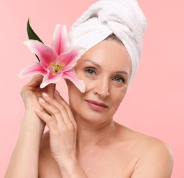 Photo of Beautiful woman with flower and towel wrapped on her head against light pink background